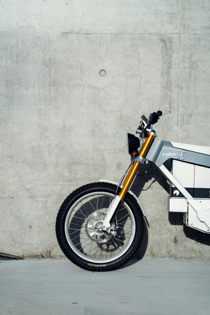 A side view of a modern electric bike leaning against a concrete wall in a minimalistic setting.
